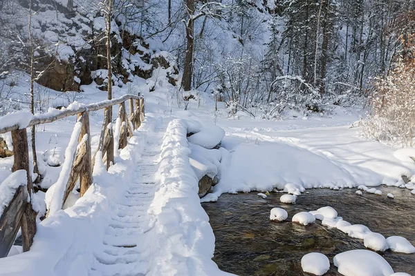 Holzbrücke über den Fluss im Schnee im Winterwald — Stockfoto