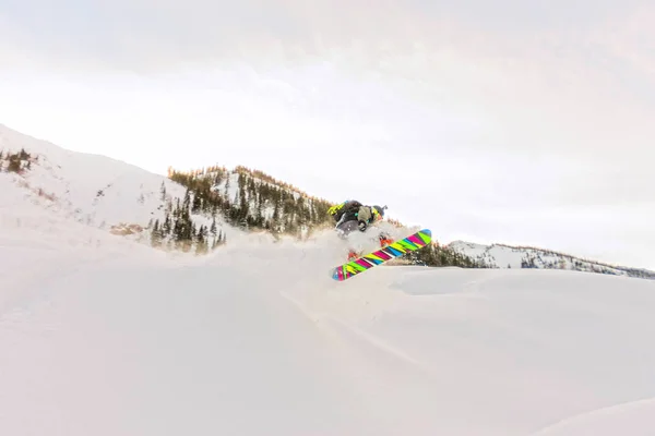 Фрирайдер прыгает в снежный спрей со склона — стоковое фото
