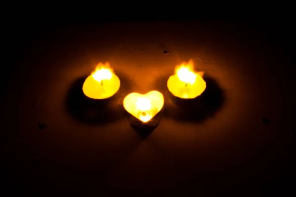 La pequeña vela redonda con un comprimido en forma de corazón se enciende en la oscuridad —  Fotos de Stock