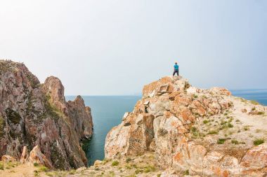 Kızıl saçlı kız deniz kenarında bir uçurumun kenarında duruyor