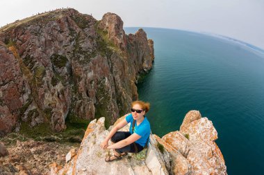 Denize yakın bir uçurumun kenarında oturan Kızıl saçlı kız