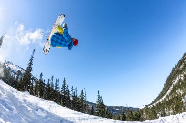 Snowboard freerider orman ve dağlar bir arka plan üzerinde bir kar rampa güneşin üzerinden atlama