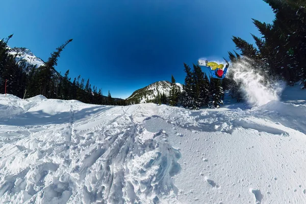 Snowboarder freerider πηδώντας από το χιόνι κεκλιμένο επίπεδο. Ευρυγώνια εναέρια Πανόραμα — Φωτογραφία Αρχείου