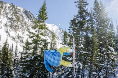 Snowboard freerider orman ve dağlar bir arka plan üzerinde bir kar rampa güneşin üzerinden atlama