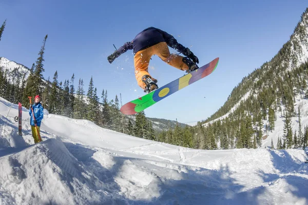 Snowboard freerider orman ve dağlar bir arka plan üzerinde bir kar rampa güneşin üzerinden atlama