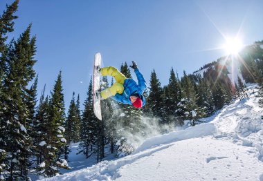 Snowboard freerider orman ve dağlar bir arka plan üzerinde bir kar rampa güneşin üzerinden atlama