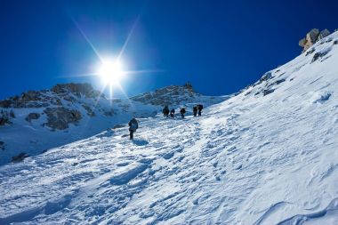 Tied climbers climbing mountain with snow field tied with a rope with ice axes and helmets clipart