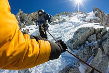 Tied climbers climbing mountain with snow field tied with a rope with ice axes and helmets first person clipart