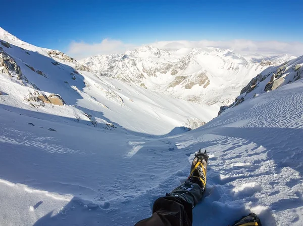 Primeira pessoa vista para as pernas em crampons ter um descanso no topo da montanha — Fotografia de Stock