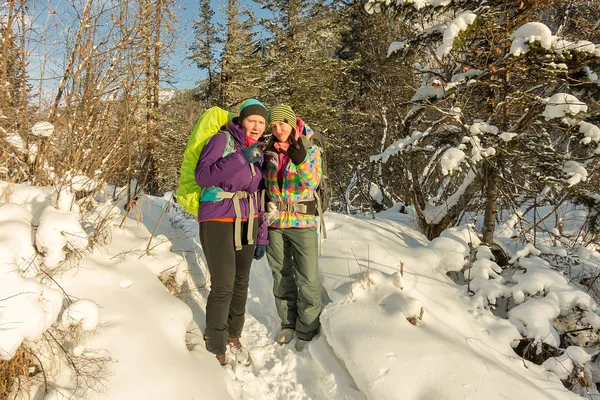 Two happy women traveler with backpacks walking in winter forest — Stock Photo, Image