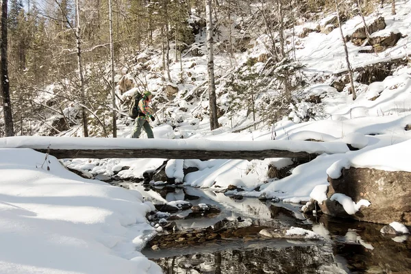 Backpacker auf einer Brücke über einen zugefrorenen Fluss im Winterwald in den Bergen — Stockfoto