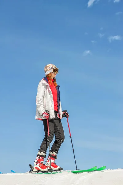Jovem no esqui alpino fica em uma pista nevada contra o céu — Fotografia de Stock