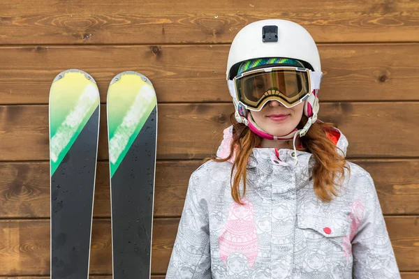 Stående kvinna skidåkare med skidor och hjälm nära trävägg — Stockfoto