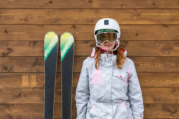 Stående kvinna skidåkare med skidor och hjälm nära trävägg — Stockfoto