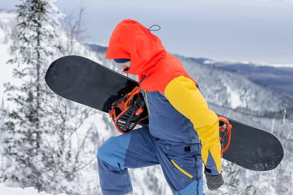 Freerider with a snowboard in overalls stands on top of a snowy mountain — Stock Photo, Image