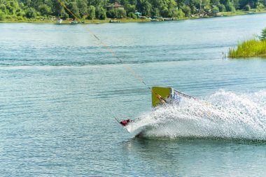 Wakeboarder bir sıçrama tahtası arkasında bir ip üzerinden atlar ve bir dalga su kılar