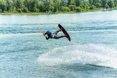 Wakeboarder bir sıçrama tahtası arkasında bir ip üzerinden atlar ve bir dalga su kılar