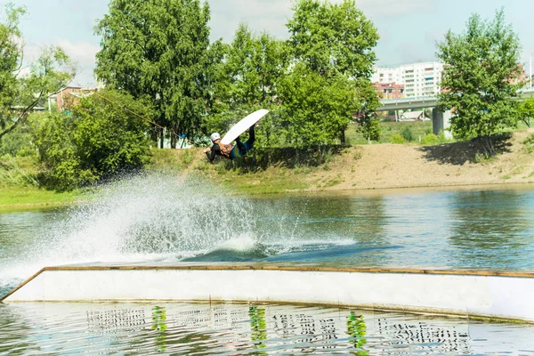 Wakeboarder salta desde un trampolín detrás de una cuerda y hace una ola en el agua — Foto de Stock