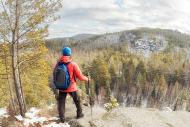 Sırt çantalı bir yürüyüşçü ormanın üstündeki dağın tepesinde duruyor ve vadiye bakıyor.