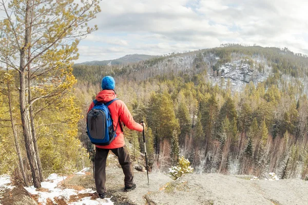 Túrázó férfi hátizsákkal áll egy hegy tetején az erdő felett, és nézi a völgyet — Stock Fotó
