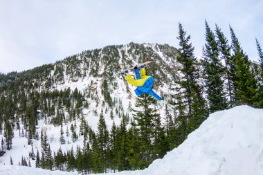 Snowboard freerider orman ve dağlar bir arka plan üzerinde bir kar rampa güneşin üzerinden atlama