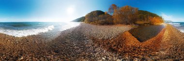 Deniz kıyısındaki çakıl taşlı kumsalın sonbahar manzarası. Gün batımında yapraklı bir körfez ve mavi bir gökyüzü. Baykal Gölü