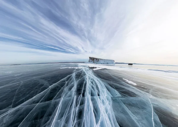 Ice of Lake Baikal w pęknięciach w pobliżu wyspy o zachodzie słońca pod szarymi chmurami. Szeroka panorama — Zdjęcie stockowe