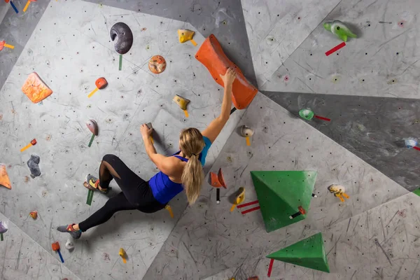 Scalatore di roccia donna appesa a una parete di arrampicata boulder, all'interno su ganci colorati Immagini Stock Royalty Free
