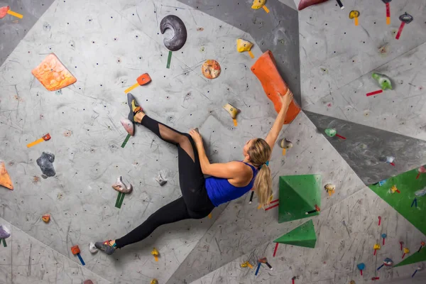 Scalatore di roccia donna appesa a una parete di arrampicata boulder, all'interno su ganci colorati Fotografia Stock