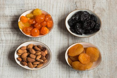 Kuruyemiş ahşap arka plan üzerinde dört tabak: kurumuş mandalina, Kuru erik, kayısı ve badem