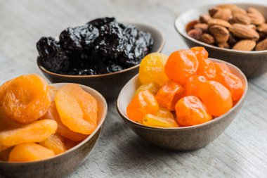 Kuruyemiş ahşap arka plan üzerinde dört tabak: kurumuş mandalina, Kuru erik, kayısı ve badem