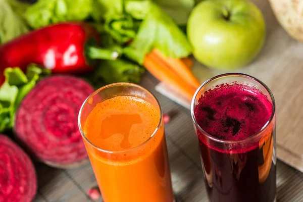 Dois copos de suco fresco diferente. Sucos de beterraba e cenoura sobre fundo de madeira cinzenta — Fotografia de Stock