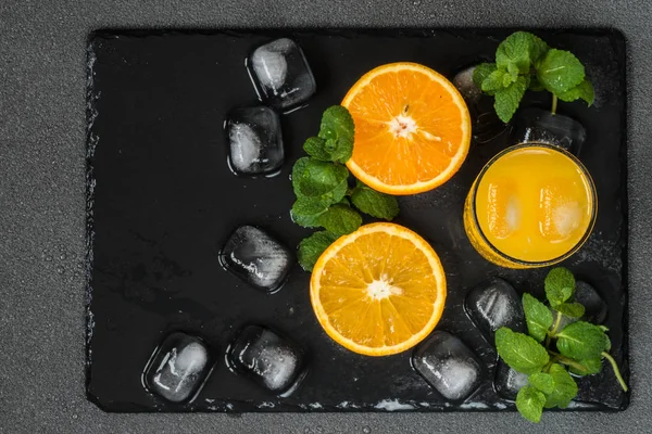 Sok pomarańczowy w szklankę blisko cytrusowych, lodu i mint na ciemnym tle — Zdjęcie stockowe