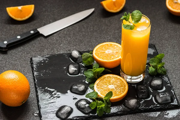 Apelsinjuice i glaset nära citrus, is och mynta på mörk bakgrund — Stockfoto