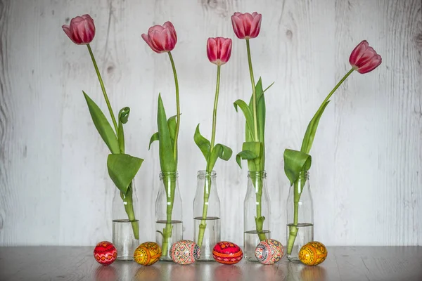 Пасхальный фон с пасхальными яйцами и розовыми тюльпанами в стеклянных бутылках на светлом деревянном фоне — стоковое фото