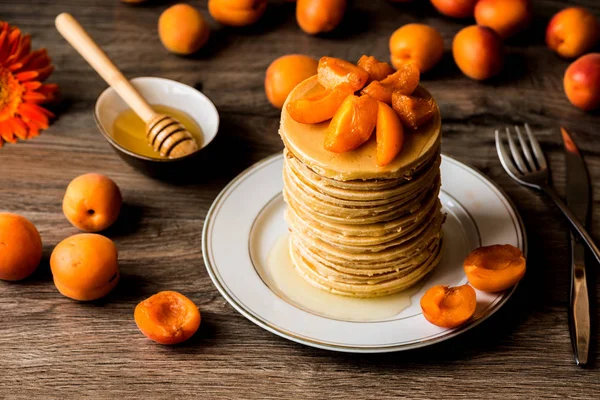 Пачка американских блинчиков с мёдом и абрикосами на деревянном фоне — стоковое фото