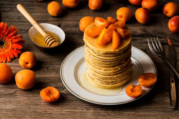 Stapel hausgemachter amerikanischer Pfannkuchen mit Honig und Aprikosen auf hölzernem Hintergrund — Stockfoto