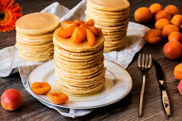 Stackes of homemade american pancakes served with honey and apricots on wooden background — Stock Photo, Image