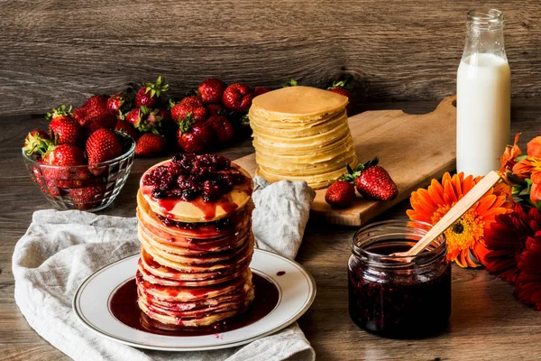 Stapel hausgemachter amerikanischer Pfannkuchen mit Marmelade und Erdbeeren auf hölzernem Hintergrund — Stockfoto