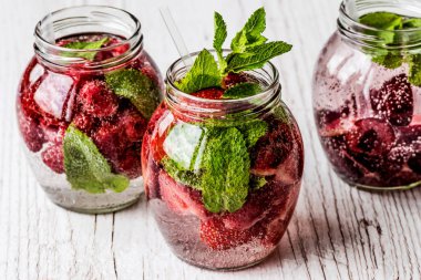 Ahududu, çilek, kiraz Beyaz ahşap zemin üzerine suyla detoks. Sağlıklı içecekler