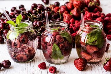 Ahududu, çilek, kiraz Beyaz ahşap zemin üzerine suyla detoks. Sağlıklı içecekler
