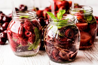 Ahududu, çilek, kiraz Beyaz ahşap zemin üzerine suyla detoks. Sağlıklı içecekler