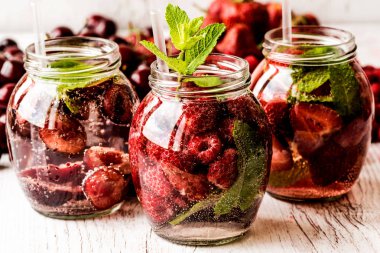 Ahududu, çilek, kiraz Beyaz ahşap zemin üzerine suyla detoks. Sağlıklı içecekler