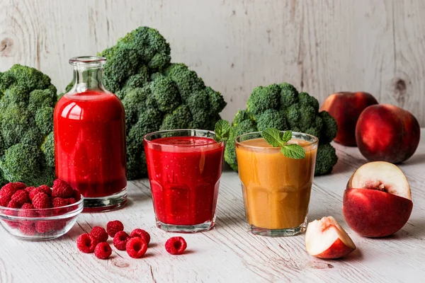 Healthy drinks. raspberry fresh smoothie in glass and bottle and peach juice on white wooden background — Stock Photo, Image