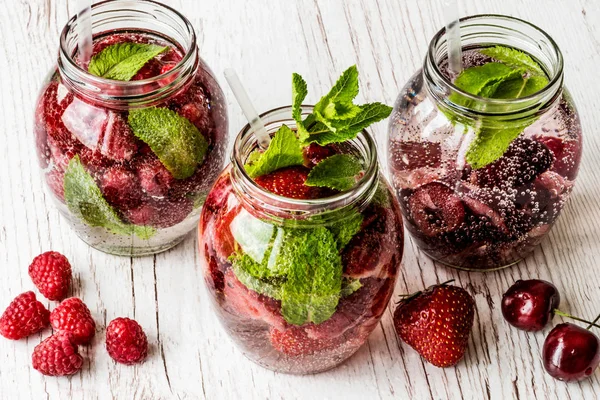 Ahududu, çilek, kiraz Beyaz ahşap zemin üzerine suyla detoks. Sağlıklı içecekler