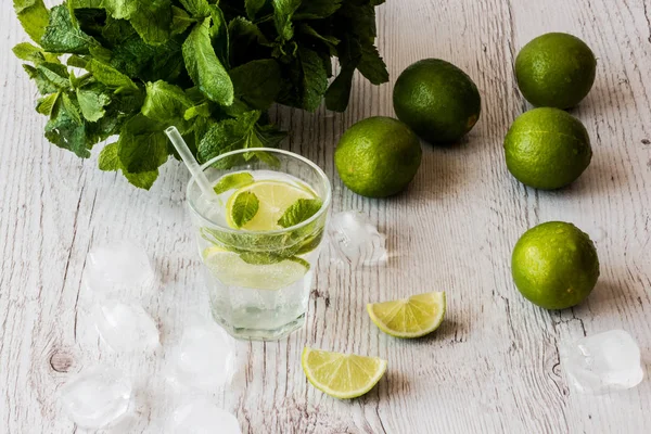 Cóctel Mojito con lima, menta y hielo sobre fondo de madera blanca . — Foto de Stock