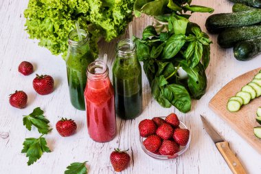 Taze yeşil smoothies ve hafif ahşap arka plan üzerinde malzemelerle çilek güler yüzlü. Sağlıklı Detoks içecekler.