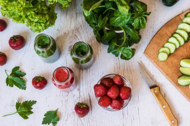 Üstten Görünüm. Taze yeşil smoothies ve hafif ahşap arka plan üzerinde malzemelerle çilek güler yüzlü. Sağlıklı Detoks içecekler.