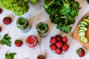 Üstten Görünüm. Taze yeşil smoothies ve hafif ahşap arka plan üzerinde malzemelerle çilek güler yüzlü. Sağlıklı Detoks içecekler.