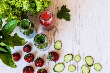 Üstten Görünüm. Taze yeşil smoothies ve hafif ahşap arka plan üzerinde malzemelerle çilek güler yüzlü. Sağlıklı Detoks içecekler.